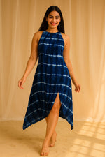 Woman walking in navy blue tie-dye halter neck asymmetrical dress with front slit and nude heels.