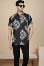 Close-up of black men’s shirt featuring white bandana medallion print, short sleeves and spread collar detail.