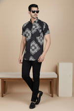 Side walking view of black printed short sleeve men’s shirt with bandana pattern, styled with black trousers and loafers.