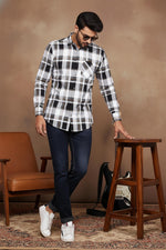 Men's black and white checkered cotton shirt standing pose, long sleeves, chest pocket, styled with dark jeans and sneakers.