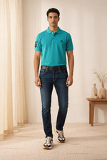 SN345 men’s turquoise cotton piqué polo t-shirt, short sleeve, collared neck, chest logo, front pose styled with jeans