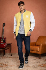 SN367 men’s pastel yellow varsity jacket with snap buttons and long sleeves, walking pose styled with jeans.