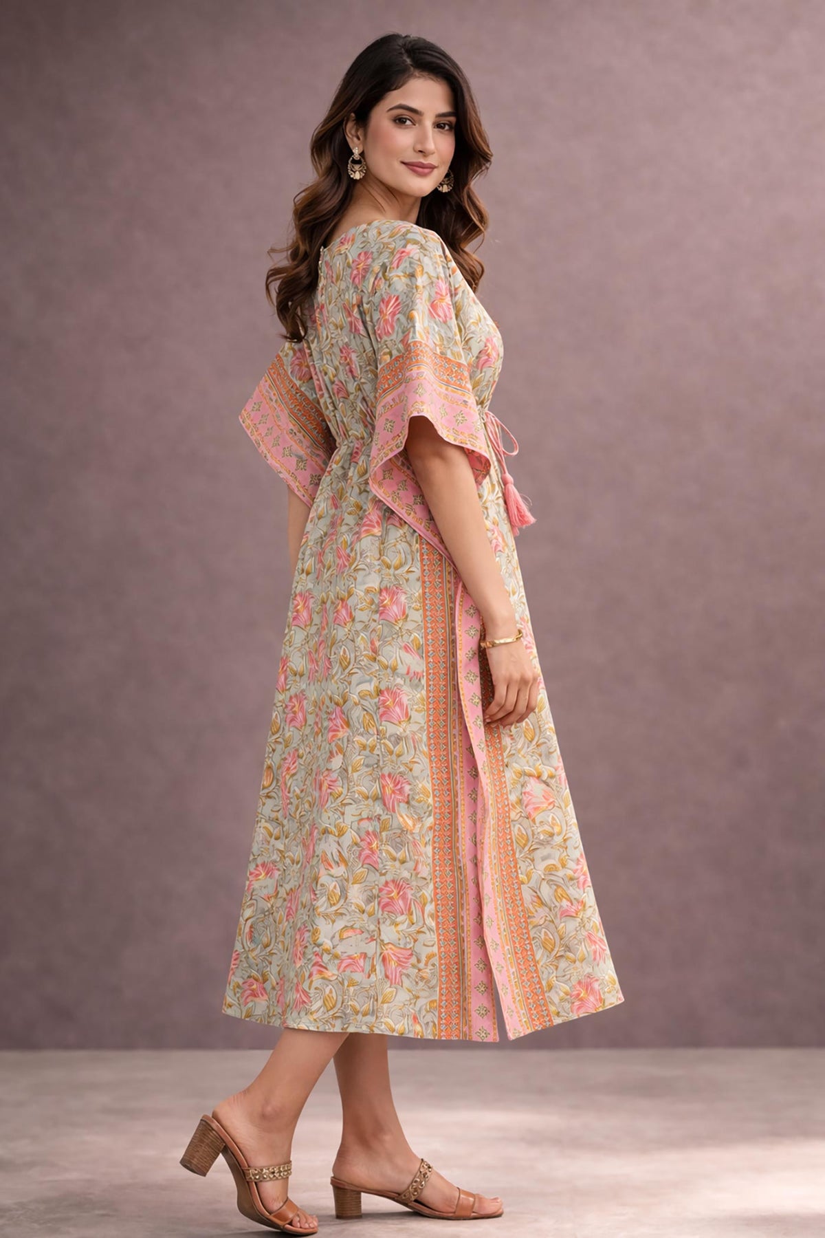 Side view of woman wearing pastel green and pink floral cotton kaftan dress with tie-up waist and border detailing