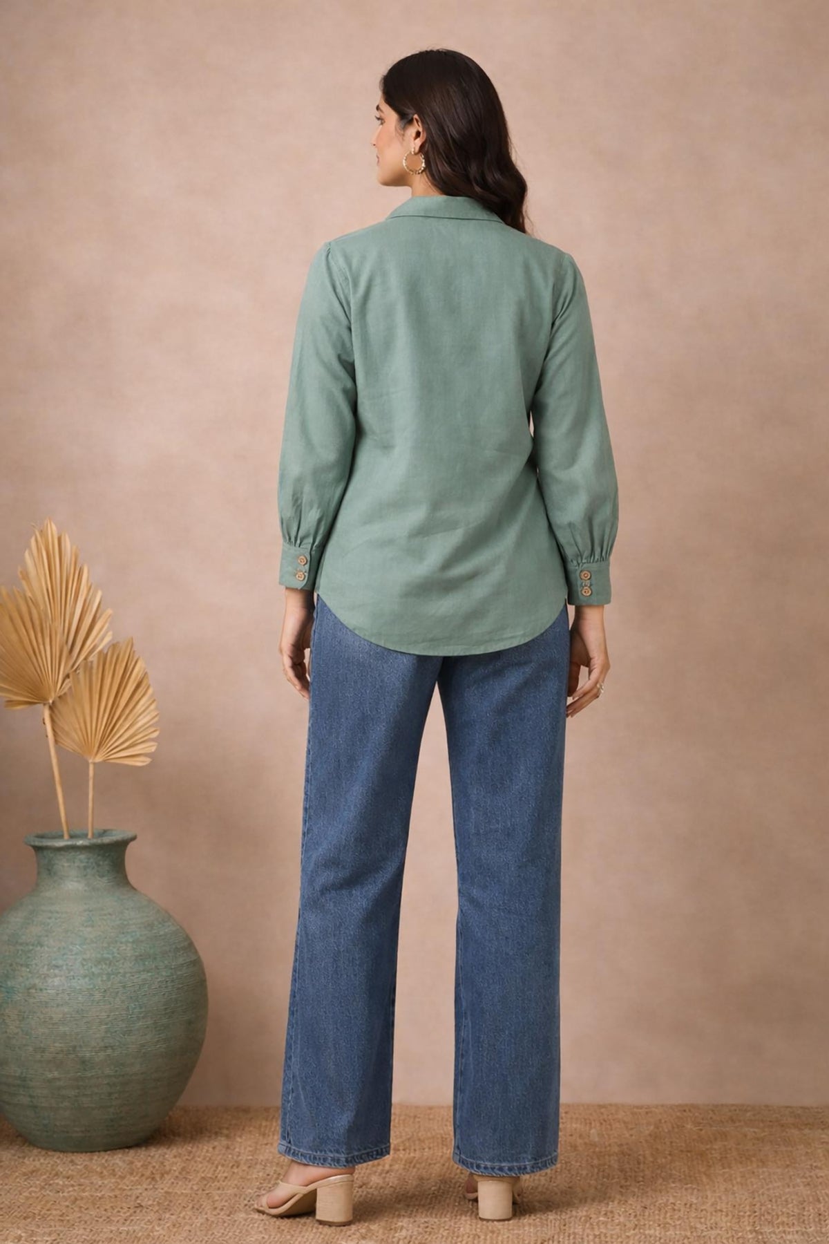 Seafoam green long sleeve blouse with curved hem, back view, styled with blue wide-leg jeans and beige block heels.