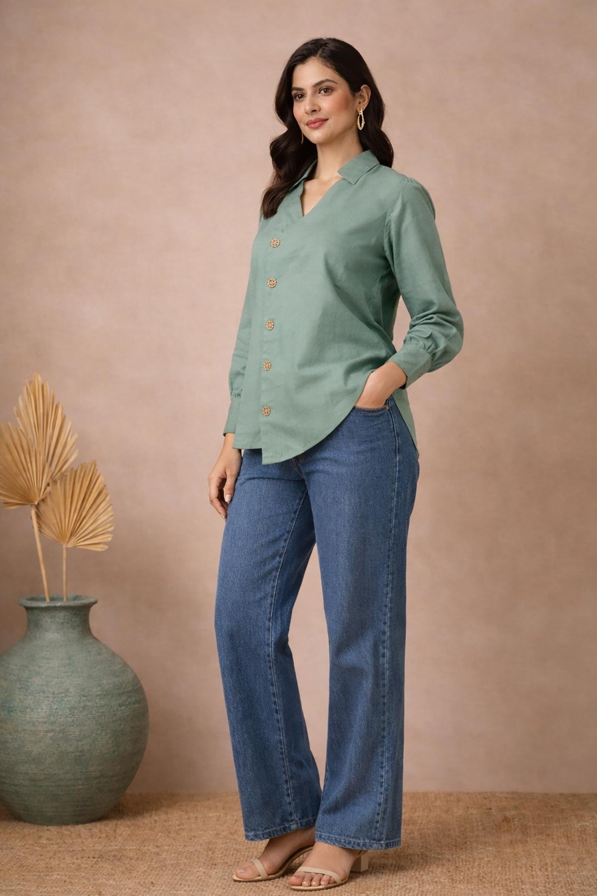 Seafoam green asymmetrical blouse side angle, long sleeves and curved hem, paired with blue jeans and block heels.