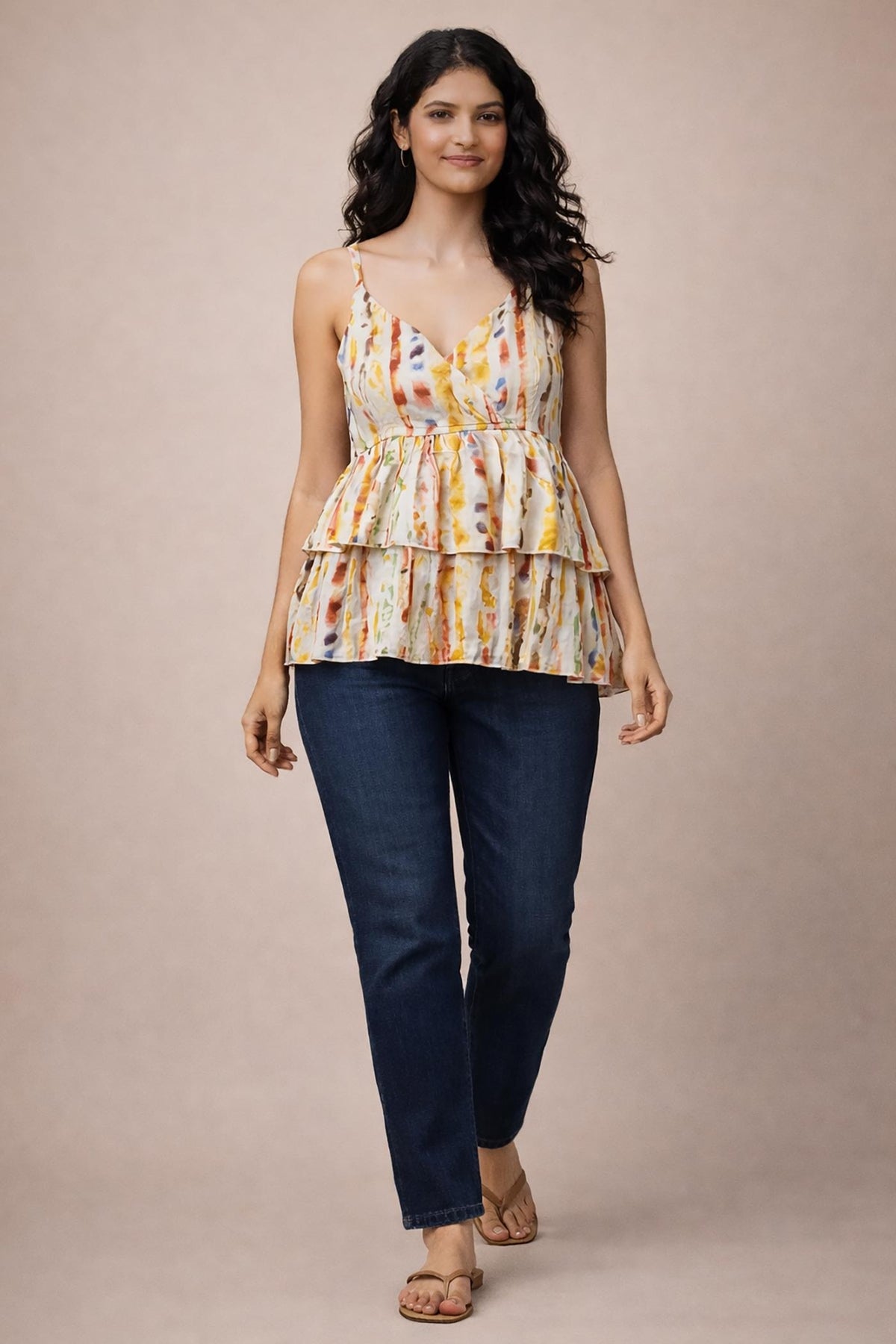 Multicolor watercolor stripe tiered camisole top with dark blue jeans, walking pose, tan sandals.