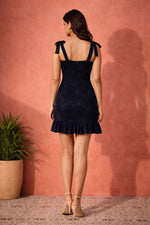 Back view of midnight navy tie-strap mini dress with square neckline, fitted silhouette, and ruffled hem detail.