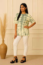 Oversized green tie-dye T-shirt side pose showing relaxed fit, short sleeves, paired with white trousers and black platform heels.