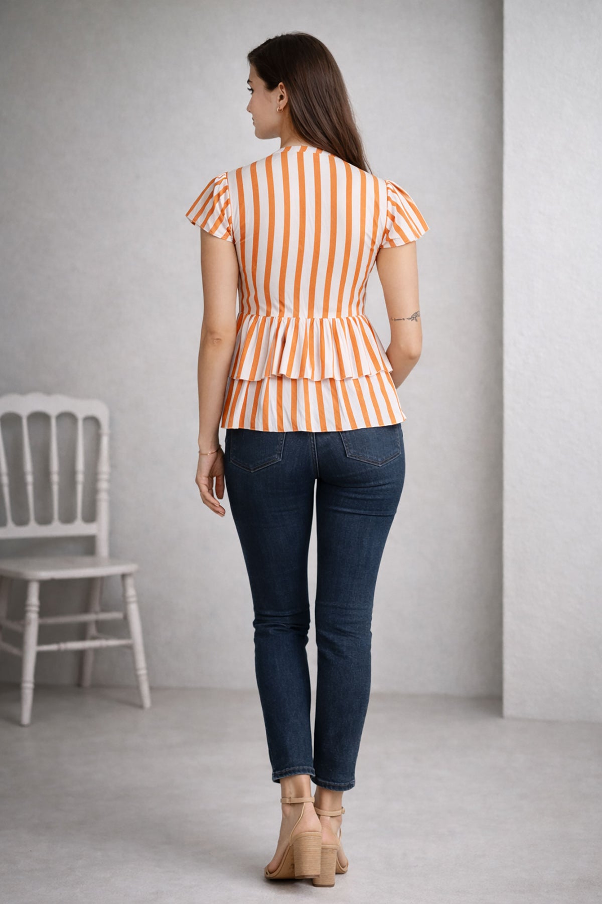 Woman wearing a striped top and dark jeans standing against a plain background