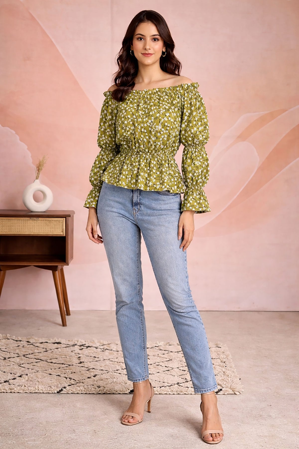 Woman wearing a green floral top and blue jeans against a pink background
