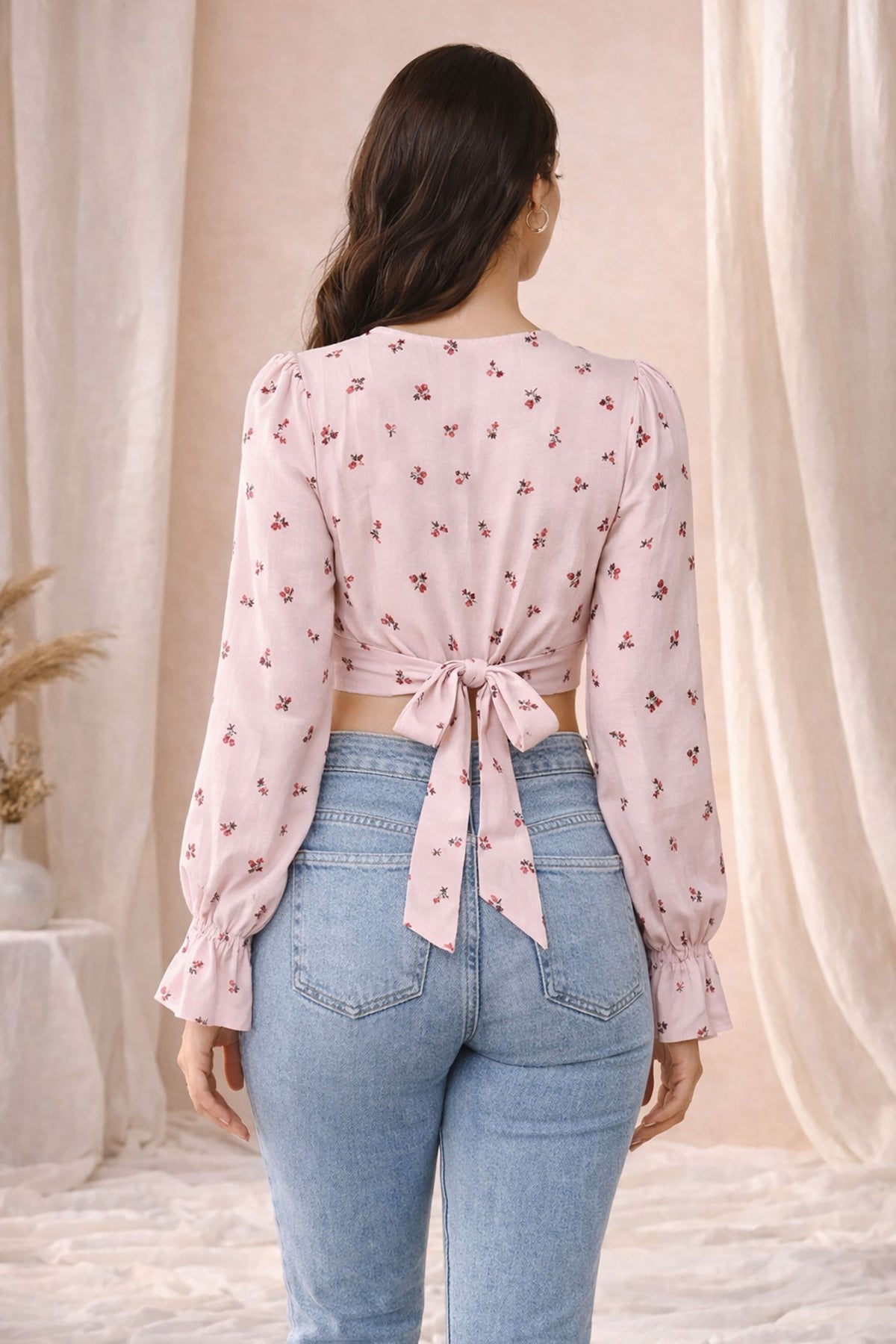Woman wearing a pink floral blouse and blue jeans with a neutral background