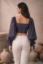 Woman wearing a patterned top and white pants standing in front of rustic vases.