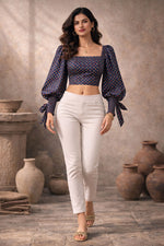 Woman wearing a dark blue patterned top and white pants standing in front of rustic vases.
