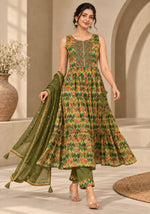 A woman models a sleeveless green and orange patterned Anarkali gown with matching green pants and a green dupatta, set against a warm beige architectural background.