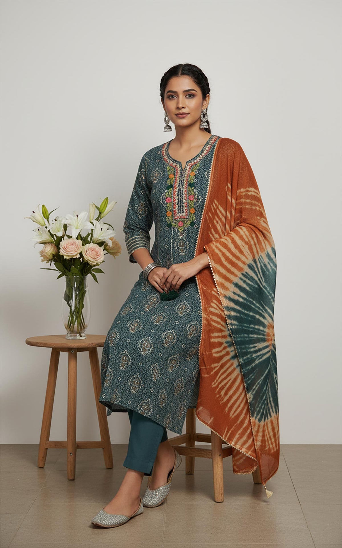 Teal ethnic kurta set with rust dupatta, relaxed fit, styled with silver juttis in seated pose.