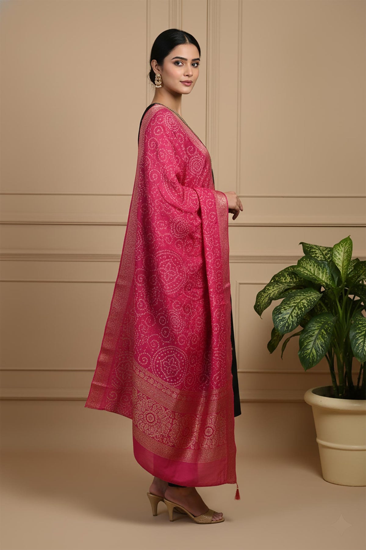 Side view of black kurta set with flowing pink bandhani dupatta and gold heels styling.