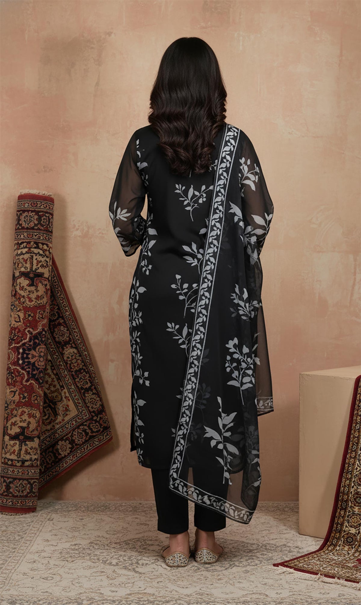 Rear view of black kurta set featuring grey floral print, sheer dupatta border, straight pants and flats.