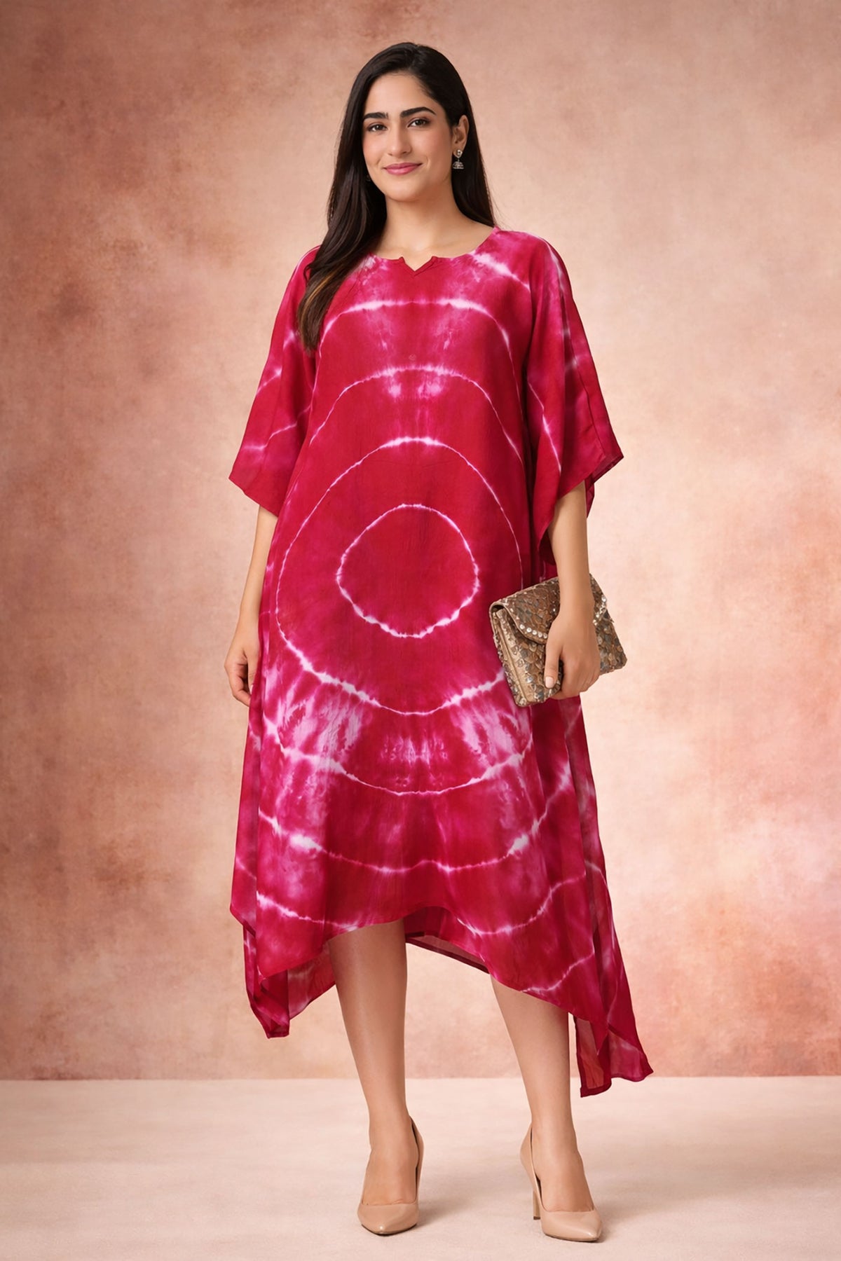 Front view of crimson tie-dye kaftan dress with V-notch neckline and flowy asymmetric hem styled with nude heels and clutch.