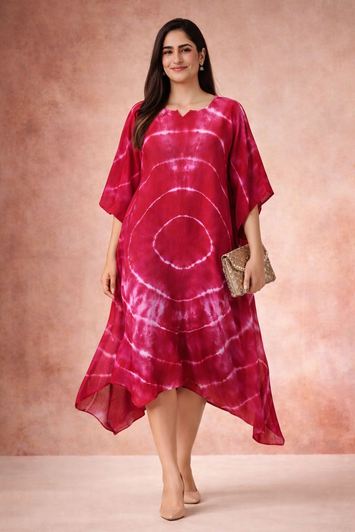 Front walking view of crimson tie-dye kaftan dress with asymmetric hem and relaxed silhouette styled with nude heels and clutch.