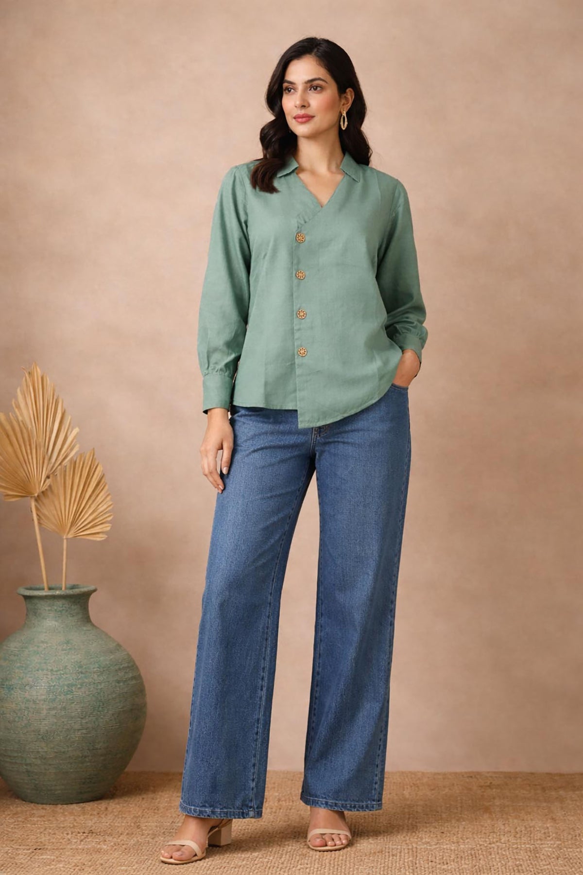 Seafoam green wrap-style blouse with wooden buttons, front view, styled with blue wide-leg jeans and neutral heels.
