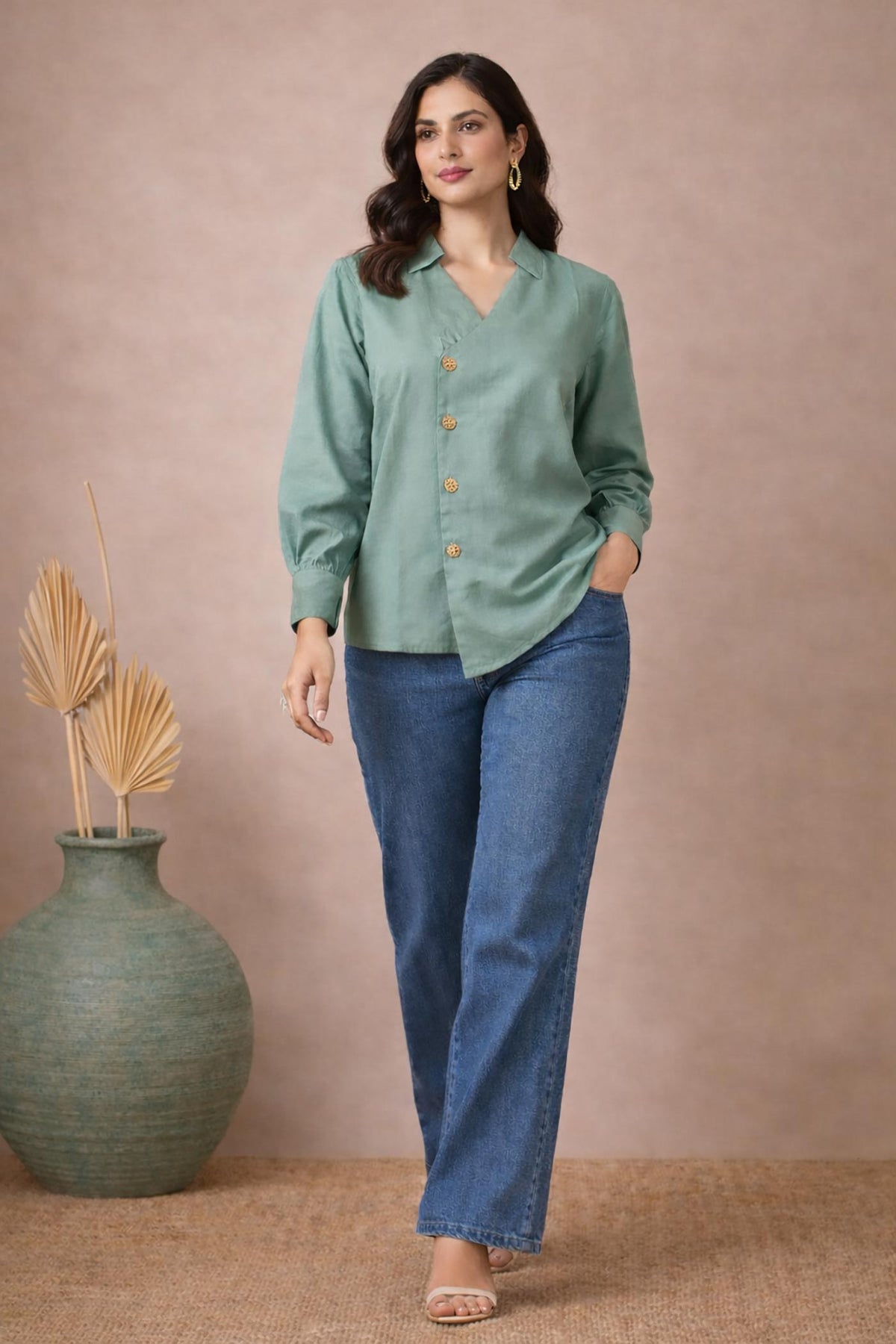 Seafoam green asymmetrical button blouse with wooden buttons, front walking view, paired with blue wide-leg jeans and block heels.