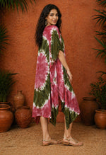 Left side three-quarter view of a South Asian female model wearing an olive and maroon tie-dye kaftan, standing against a warm terracotta textured wall with clay pots and greenery in soft studio lighting.