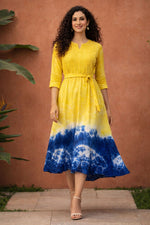 Woman walking in yellow and blue tie-dye cotton midi dress with waist belt and three-quarter sleeves