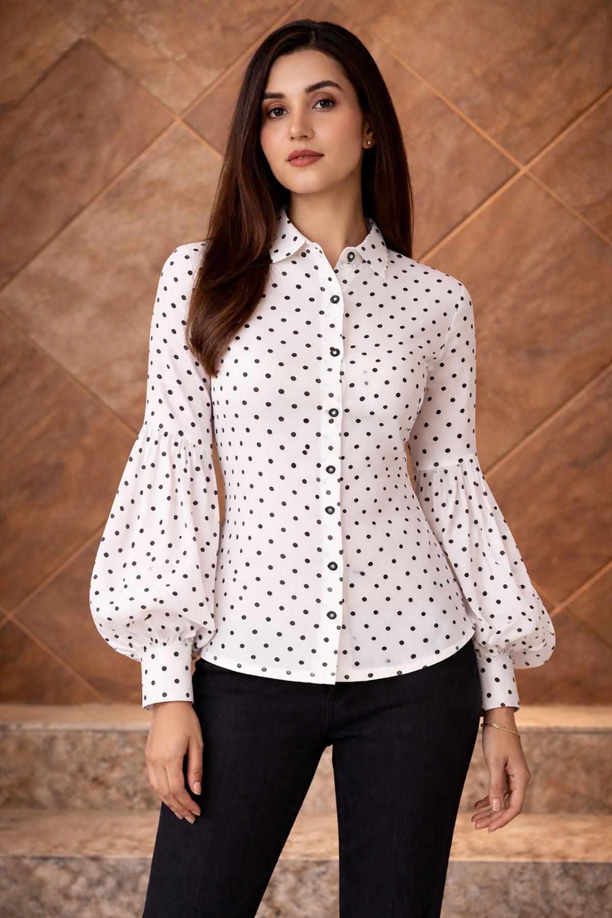 Woman wearing a white blouse with black polka dots against a wooden paneled wall.