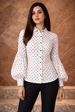Woman wearing a white blouse with black polka dots against a wooden paneled wall.