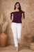 Woman wearing a purple off-shoulder top and white pants against a brown textured wall.