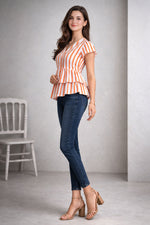 Woman wearing a striped peplum top and blue jeans standing against a plain background
