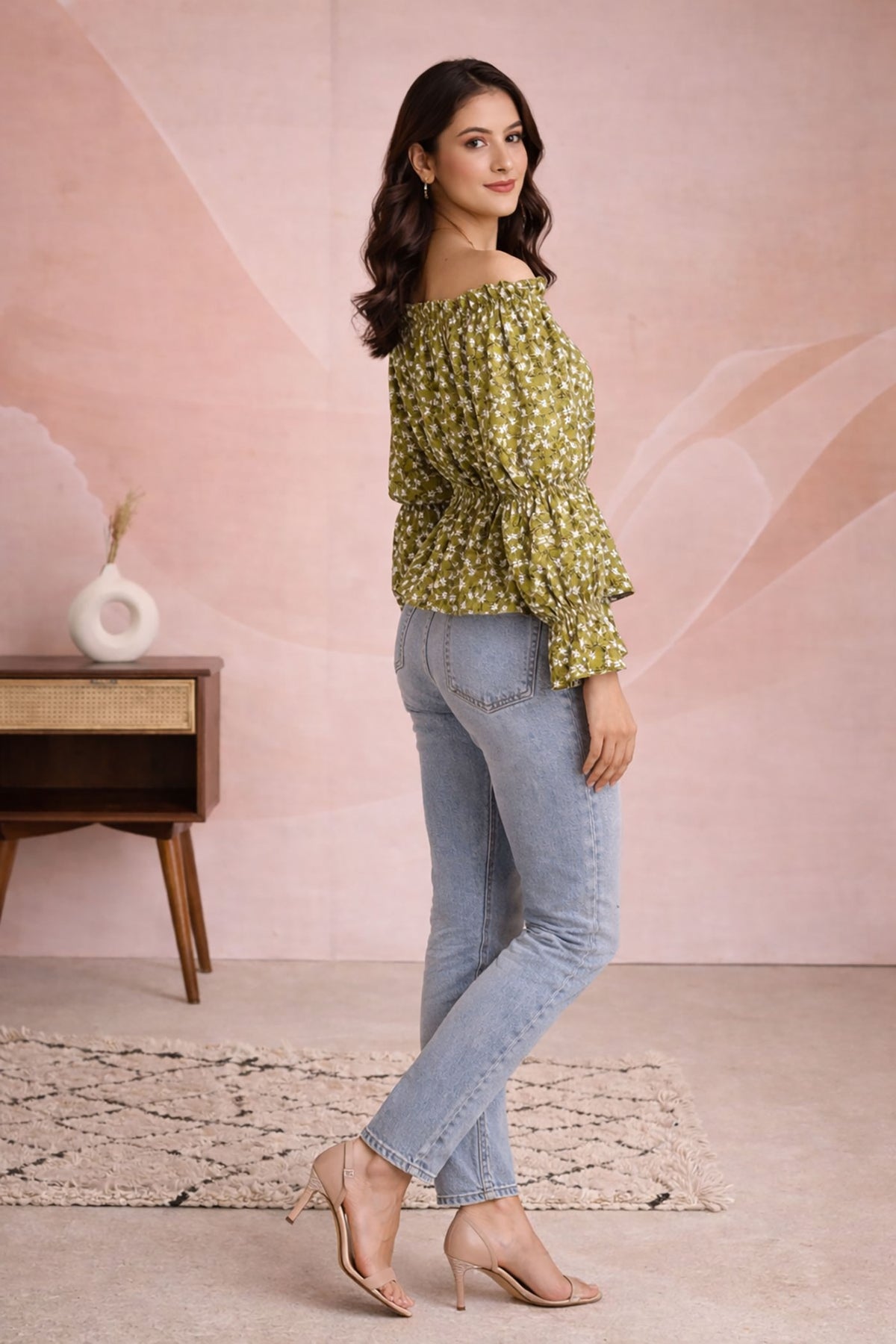 Woman wearing a green floral blouse and blue jeans against a pink wall.