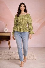 Woman wearing a green floral off-shoulder top and blue jeans against a pink wall.