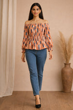 Woman wearing an off-shoulder top with geometric pattern and blue jeans against a beige wall.