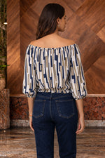 Woman wearing a patterned top and dark jeans against a wooden wall.