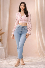 Woman wearing a pink floral blouse and blue jeans against a beige curtain background