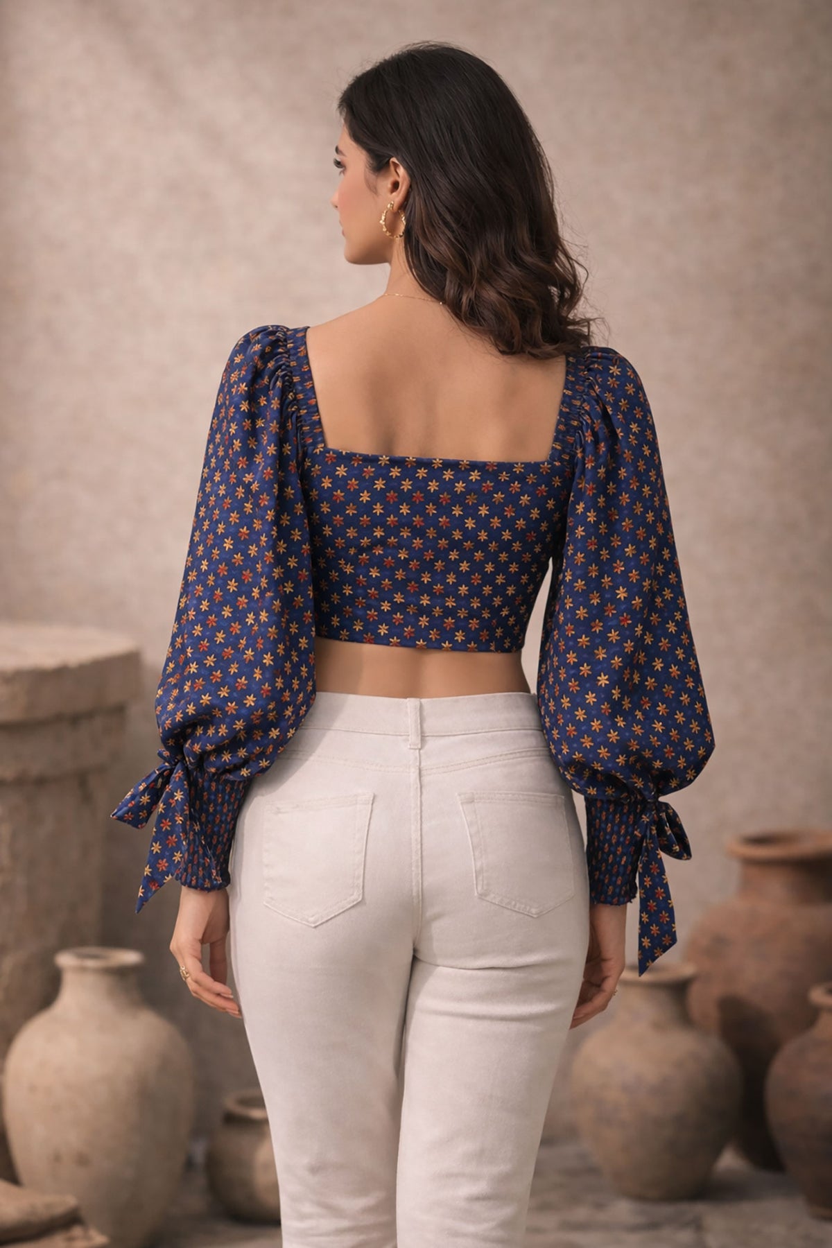 Woman wearing a patterned top and white pants standing in front of rustic vases.