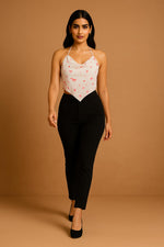 White halter neck crop top with red star print and pointed hem, front walking view with black fitted pants.